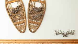 Een kamer met een houten lambrisering, een ronde tafel met een lamp, en sneeuwschoenen en gewehoorns bevestigd aan de muur.