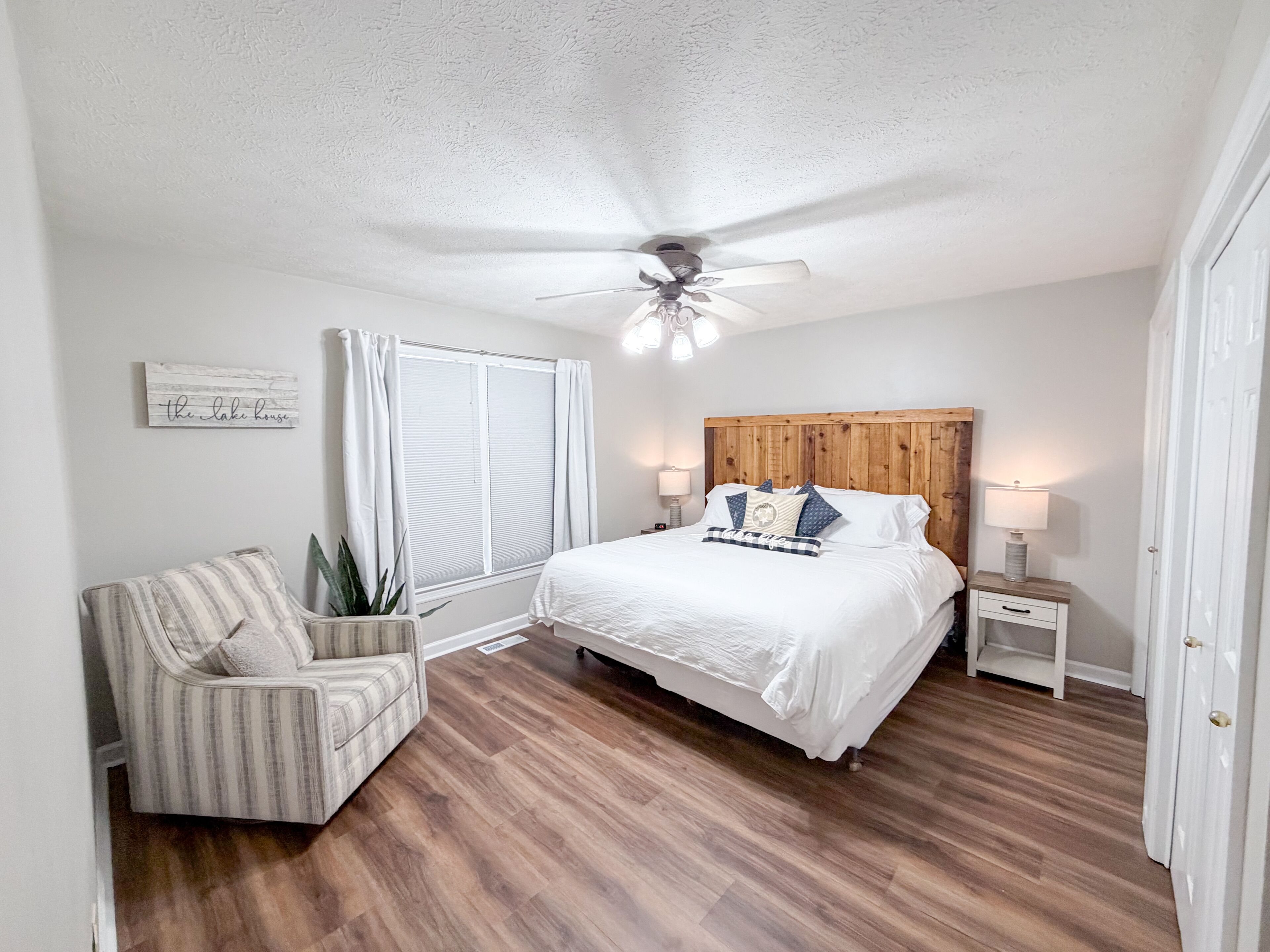 A bedroom with a bed, a chair, a nightstand, a ceiling fan, and a window with curtains.