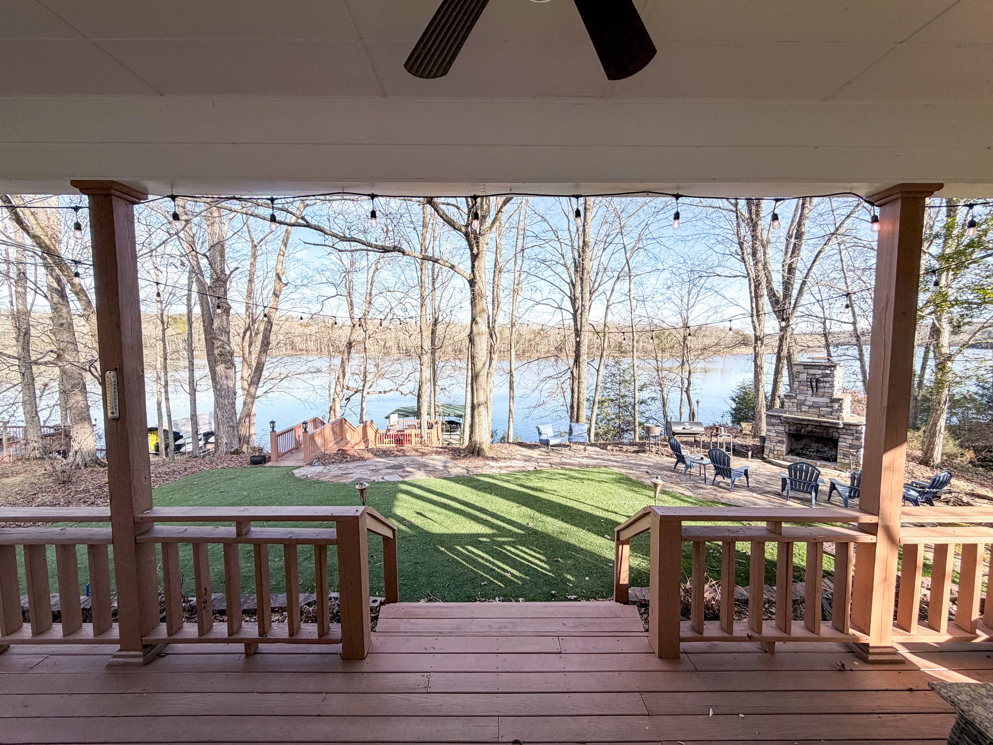 A covered deck with a view of a lake, a grill, and outdoor seating.
