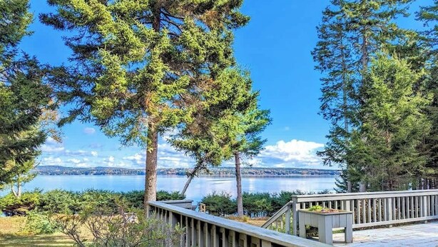 Une terrasse en bois dotée d’une rambarde, qui offre une vue sur un lac et une zone boisée.