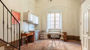 Une cuisine avec un sol en pierre, des meubles blancs, un radiateur et une fenêtre.