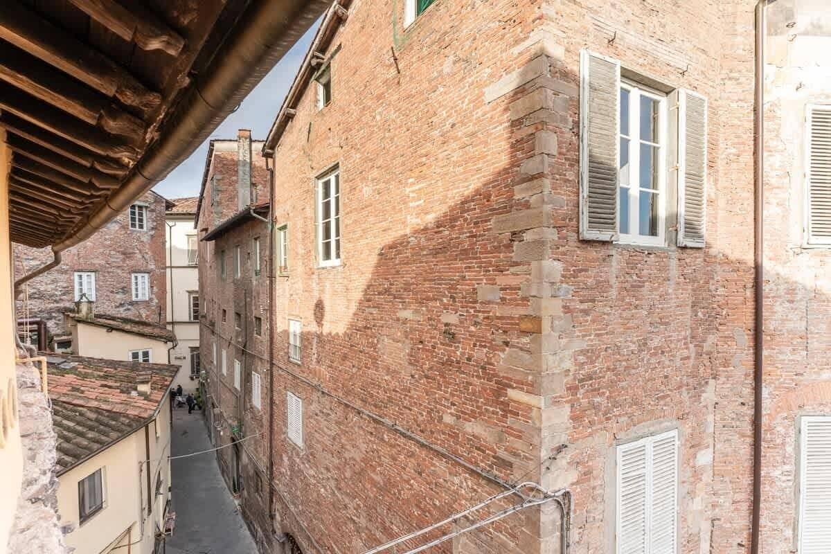 A narrow alleyway between buildings with brick facades and white shutters.