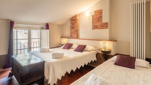 A bedroom with two beds, a brick accent wall, a radiator, and a window with curtains. - Room Flavia all'Anfiteatro - Affitti Brevi Italia (Lucca)