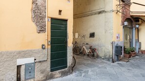 A narrow street with a building featuring a green door, a utility box, and a bicycle parked outside. - Room Flavia all'Anfiteatro - Affitti Brevi Italia (Lucca)