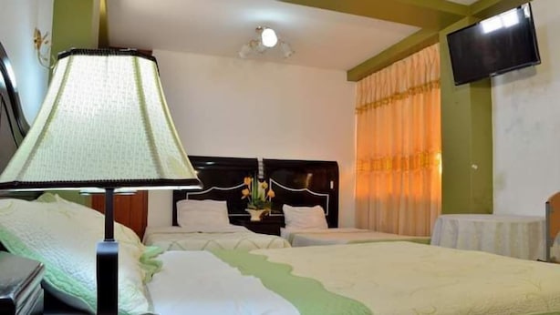 A hotel room with two beds, a nightstand, a lamp, a TV, and a window with curtains. - Hostal Mansion Dorada (Tacna)