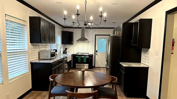 A modern kitchen with a central island, black cabinetry, and a chandelier.