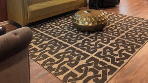 A living room with a sofa, ottoman, and a patterned rug.