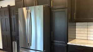 A kitchen with dark wooden cabinets, a stainless steel refrigerator, and a tiled backsplash.
