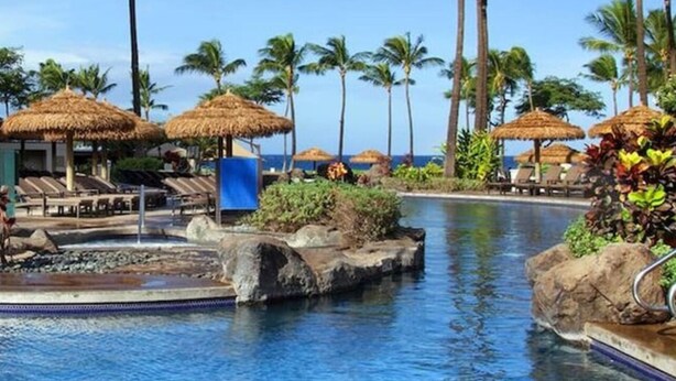 A resort pool area with thatched umbrellas, lounge chairs, and palm trees. - Ocean Front Westin Villas North!  Gorgeous Pools, Beach & Amenities! (Lahaina)