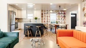 Une cuisine moderne avec des meubles blancs, un îlot central doté de tabourets et un mur décoratif orné de visages de dessins animés.
