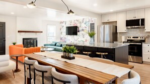 Une cuisine moderne dotée d’un îlot central, d’appareils électroménagers en acier inoxydable et d’un coin repas avec une table et des chaises en bois.