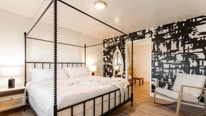 Un lit à baldaquin avec du linge de lit blanc, un plancher en bois, un fauteuil à bascule et une fresque murale abstraite en noir et blanc.