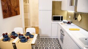 Une cuisine moderne avec des meubles blancs, un four à micro-ondes et un sol à motifs. On y trouve une table à manger dressée avec des bols bleus et des pommes.
