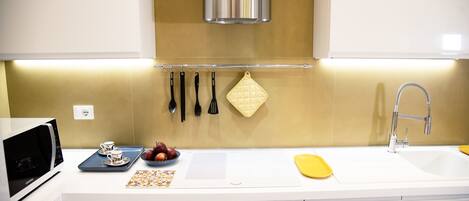 A modern kitchen with white cabinetry, a stainless steel range hood, a microwave, a sink, and a countertop with a cutting board, a bowl of fruit, and a tray with cups and saucers.