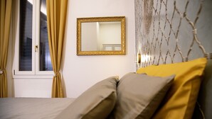 Une chambre à coucher avec un lit, une fenêtre avec des rideaux, un miroir et un mur décoré d’un motif.