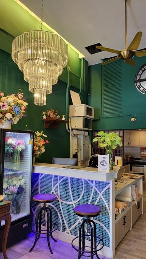 Een bar met een groene wand, een kroonluchter, een plafondventilator, een klok en een koelkast met bloemen.