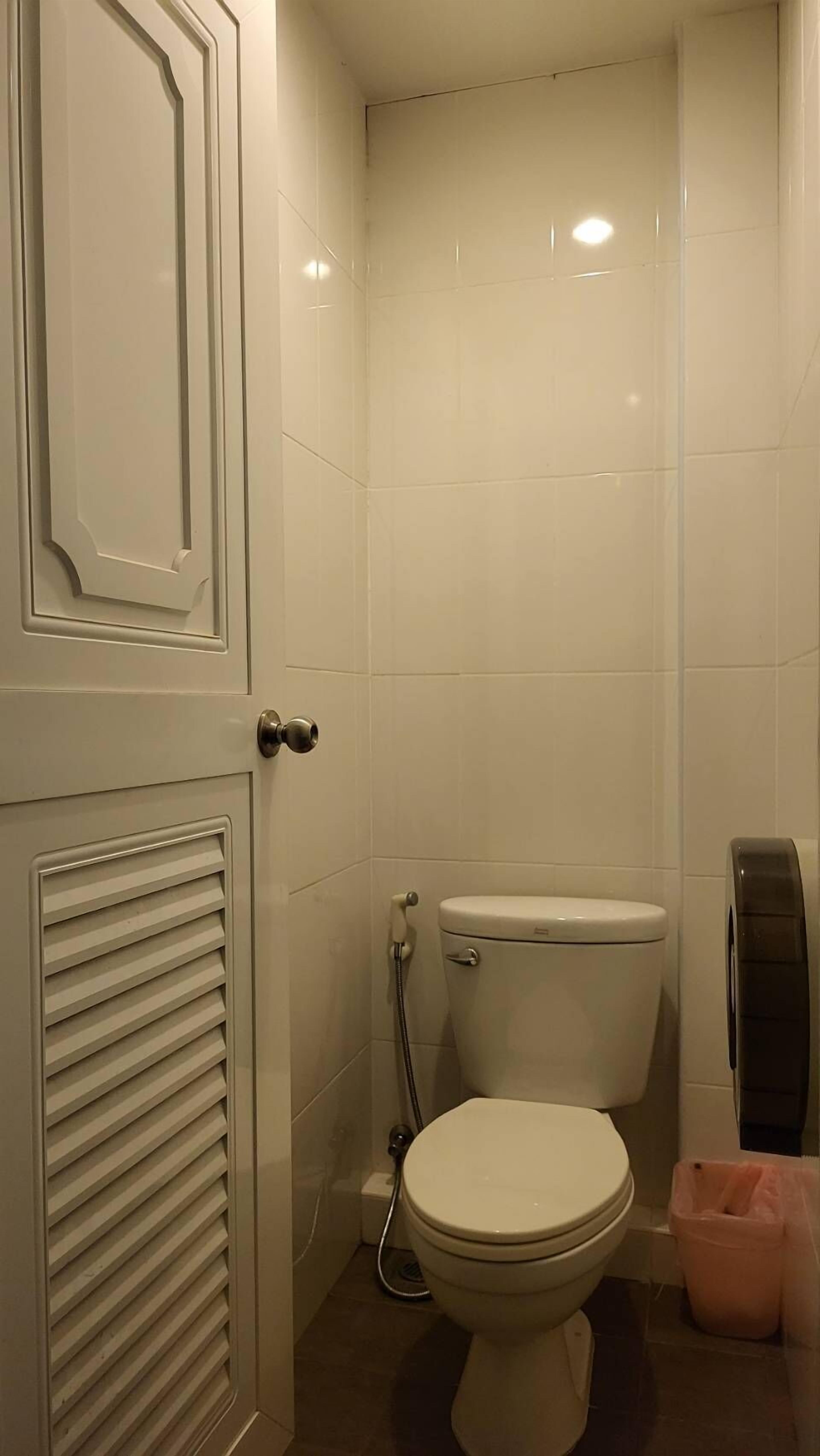 A small, clean bathroom with a toilet, a hand dryer, and a trash bin.