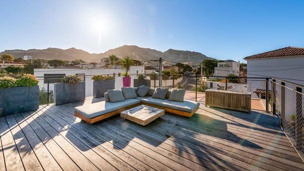 Une terrasse sur le toit, dotée d’un canapé d’angle et d’une table basse, entourée de jardinières et offrant une vue sur le paysage urbain, avec des montagnes en arrière-plan.