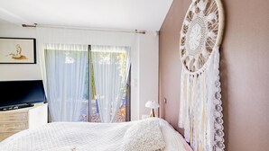 Une chambre à coucher avec un lit, un attrape-rêves, une télévision et une fenêtre avec des rideaux.