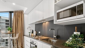 Une cuisine moderne avec des armoires blanches, un évier en acier inoxydable et un four à micro-ondes. On y trouve un coin repas avec une table et des chaises, ainsi qu’une plante posée sur le comptoir.