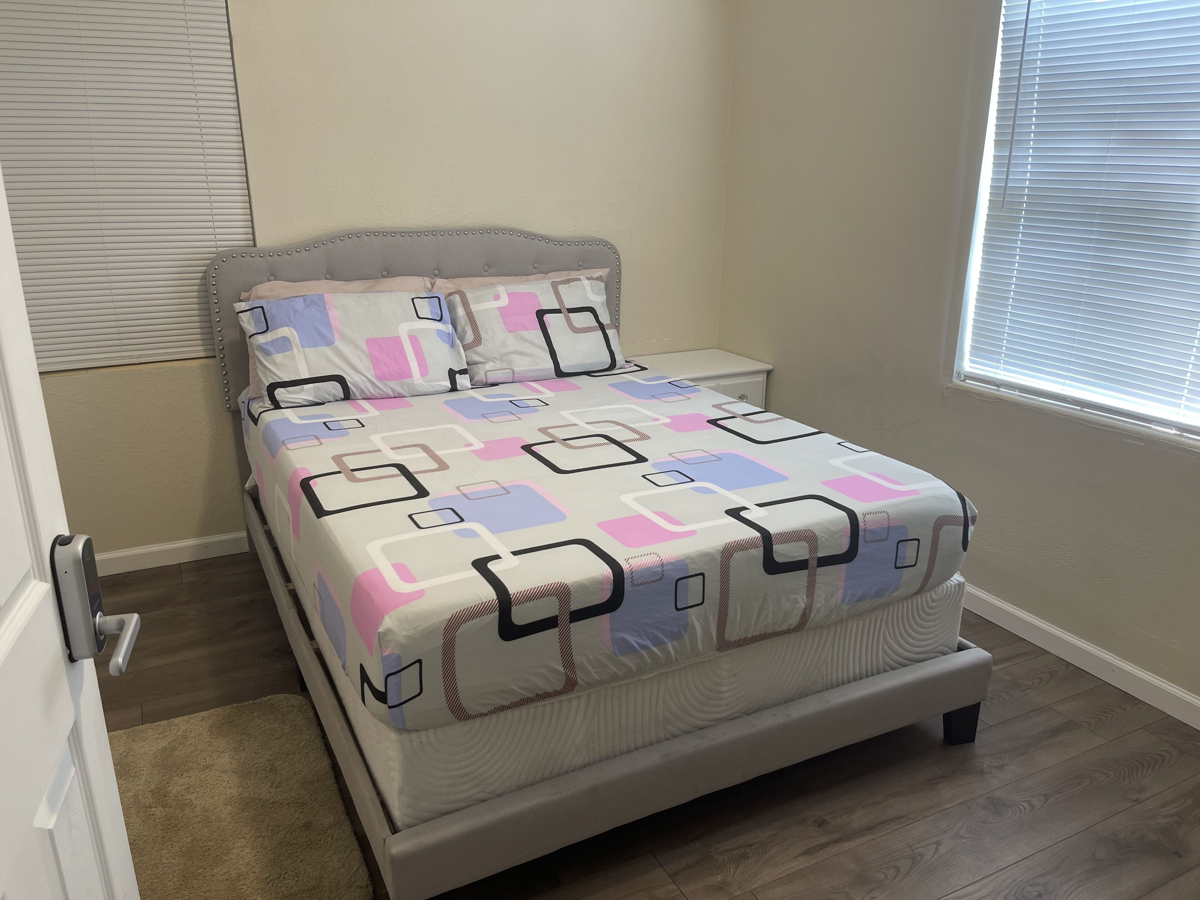 A neatly made bed with a geometric patterned bedspread, a headboard, and a nightstand with a lamp.