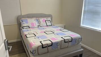 A neatly made bed with a geometric patterned bedspread, a headboard, and a nightstand with a lamp.
