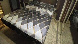 Un dormitorio pequeño con cama, cabecera, lámpara de techo y puerta.