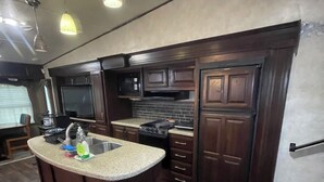 Una cocina con armarios de madera oscura, una isla con cubierta de granito, un lavamanos de acero inoxidable y un microondas empotrado.