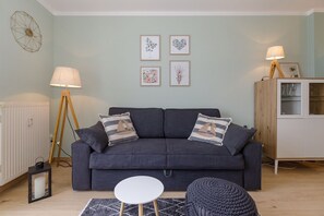 Un salon moderne avec un canapé gris foncé, deux coussins assortis, une petite table ronde et un lampadaire.