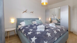 A modern bedroom with a bed featuring a star-patterned blanket, a bedside table, a hanging light fixture, and a wardrobe with a mirror.