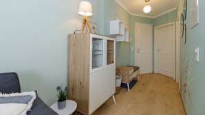 A compact living space with a wooden cabinet, a small table with a plant, a lamp, and a door leading to another room.