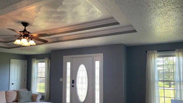 Un salon avec un canapé beige, un ventilateur de plafond et une porte ornée de panneaux de vitrail.