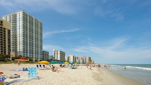 Een strand met wolkenkrabbers op de achtergrond, strandparasols en ligstoelen.