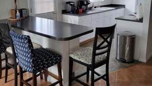Une cuisine moderne avec des meubles blancs, un plan de travail noir et un îlot central. On y trouve deux chaises avec un revêtement à motifs et une poubelle.