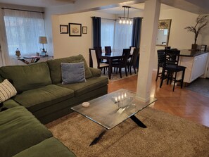 Una sala de estar con un sofá verde, una mesa de centro de vidrio y una zona de comedor con mesa y sillas.