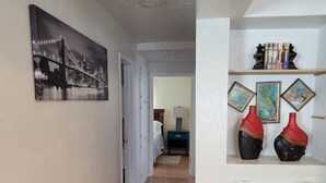 Un couloir doté d’un plancher en bois, d’un mur blanc orné d’une photographie en noir et blanc, et d’un autre mur blanc sur lequel sont accrochées trois peintures encadrées et deux vases rouges.