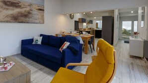 Una sala de estar moderna con un sofá azul, un sillón amarillo y una zona de comedor con una mesa de madera.
