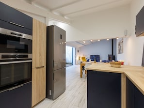 Une cuisine moderne dotée d’appareils électroménagers intégrés, un coin repas avec une table et des chaises, et une grande fenêtre laissant entrer la lumière naturelle.