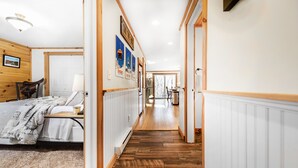A hallway with a wooden floor, white walls, and a bed with a patterned bedspread.