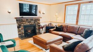 A living room with a stone fireplace, leather sofa, and a television mounted above it.