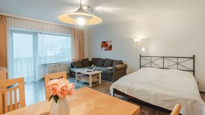 A hotel room with a bed, a sofa, a dining table with chairs, a vase of flowers, and a ceiling light fixture. - Landhaus St. Georg by Interhome (Bad Gastein)