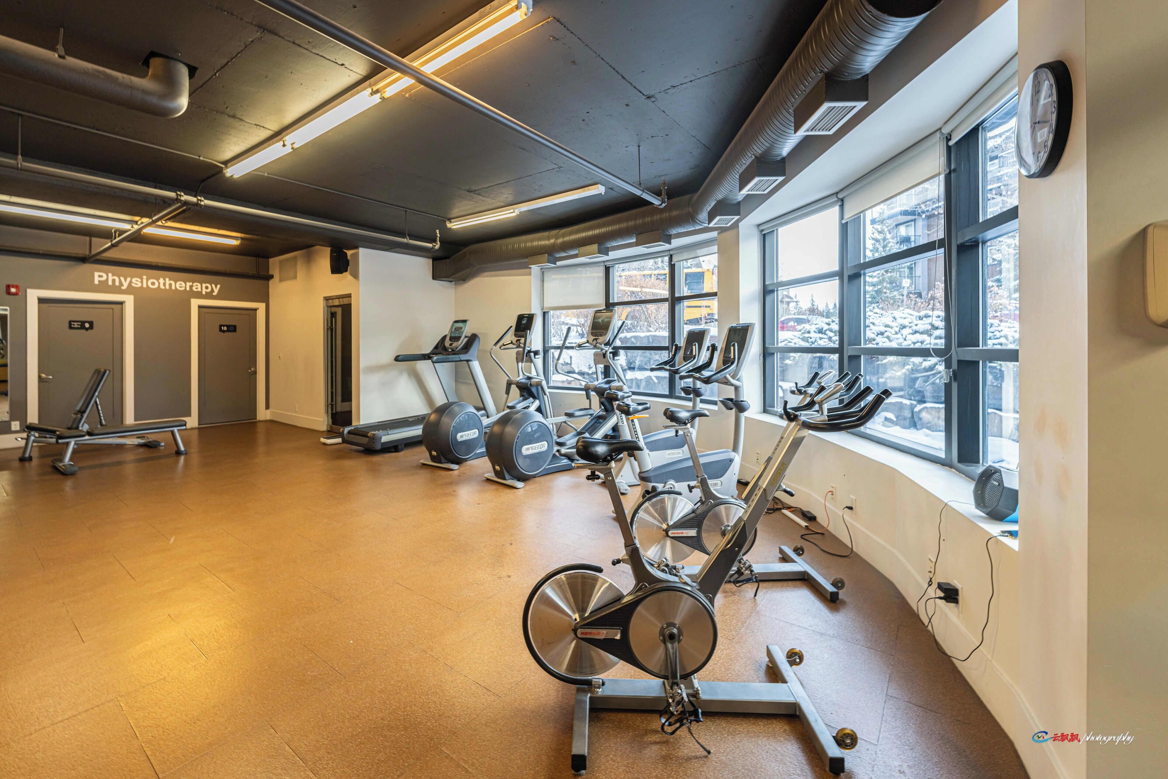Ein Fitnessraum mit Cardiogeräten, einem Physiotherapieraum und großen Fenstern.