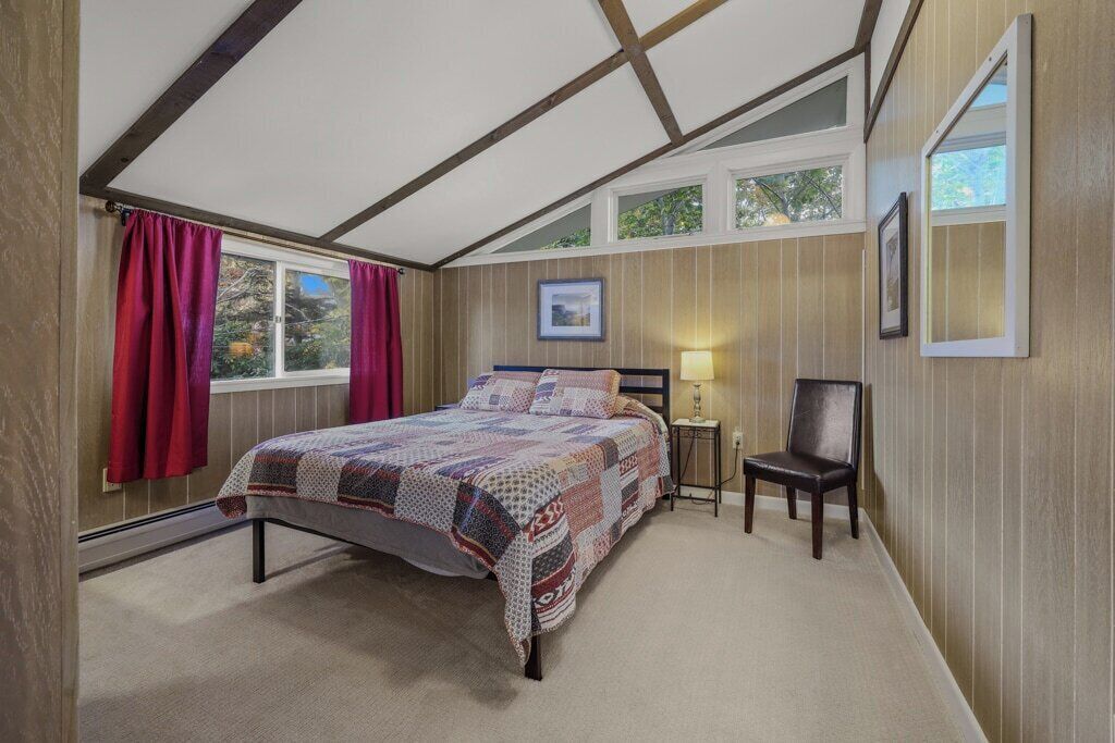 A bedroom with a bed, a chair, a nightstand, and a window with curtains.