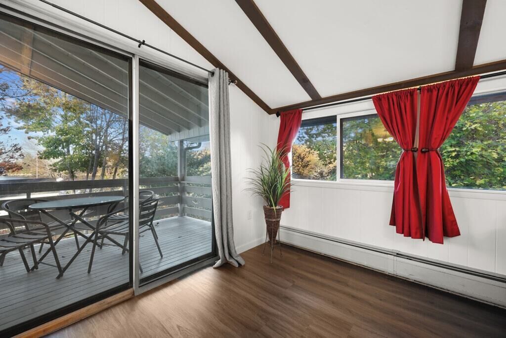 Quarto com porta de vidro deslizante que dá para um deck externo, uma planta em vaso e uma janela com cortinas vermelhas.