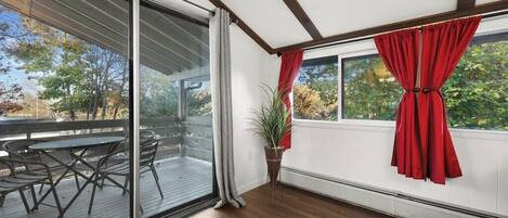 Quarto com porta de vidro deslizante que dá para um deck externo, uma planta em vaso e uma janela com cortinas vermelhas.