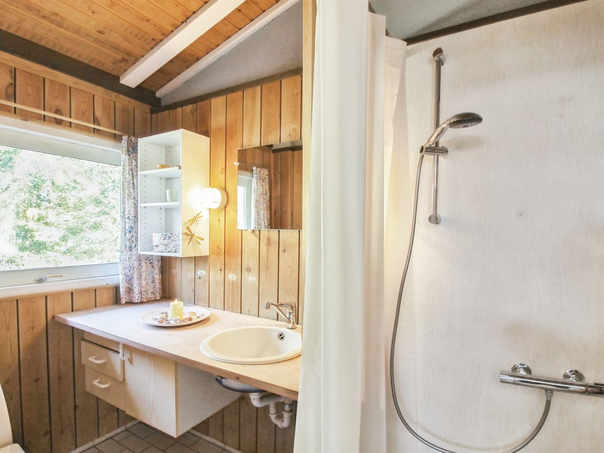 Une salle de bain avec des lambris en bois, un lavabo, un miroir et une douche.