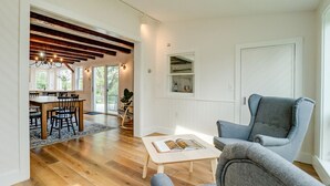 A spacious living room with a wooden floor, a dining area with a table and chairs, and a large window.