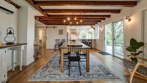A spacious dining area with a wooden table and chairs, a patterned rug, and exposed wooden beams on the ceiling.
