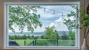 A window with a view of a green landscape, a clear sky, and a distant body of water.