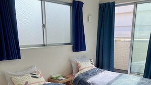 Une chambre avec deux lits, une fenêtre avec des rideaux, une table de chevet avec une lampe, et une vue sur l’extérieur.